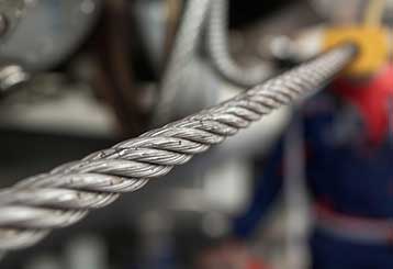 Detailed view of a thick metal garage door cable with technician working in the background in Anaheim garage