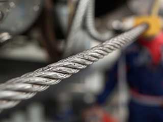 Detailed view of a thick metal garage door cable with technician working in the background in Anaheim garage