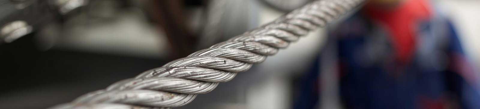 Detailed view of a thick metal garage door cable with technician working in the background in Anaheim garage