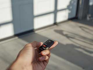 Close-up of a person using a modern garage door remote opener, with blurred white garage doors in the background