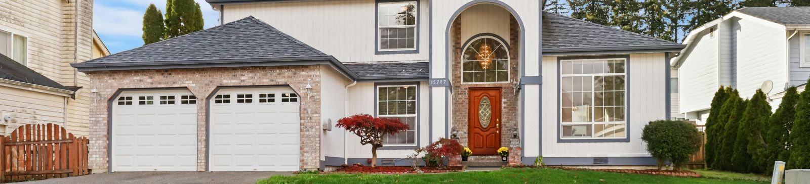 Front view of a house in Anaheim with two white garage doors, landscaped yard, and welcoming entrance, representing reliable garage door repair services