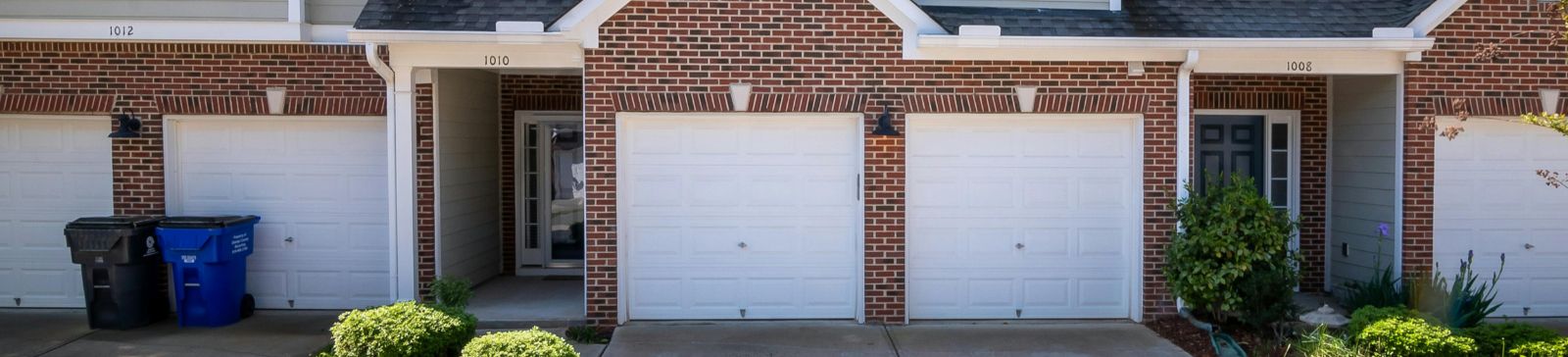 Three suburban Anaheim townhome garages with white paneled doors and tidy landscaping, representing garage door solutions and advice for local homeowners