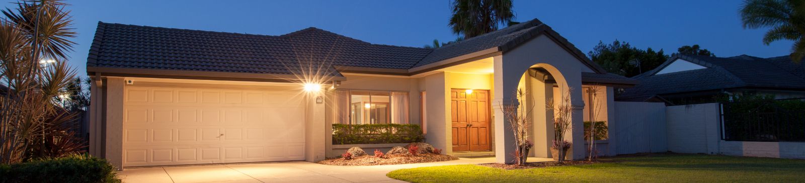 Brightly lit garage and home exterior at dusk in Anaheim, illustrating reliable garage door opener service and maintenance tips