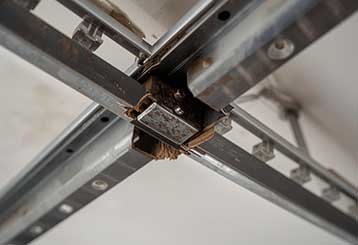 Damaged and misaligned metal garage door tracks showing rust and wear on a residential garage ceiling