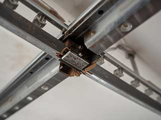 Damaged and misaligned metal garage door tracks showing rust and wear on a residential garage ceiling